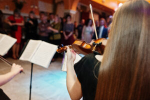 Close up portrait of a beautiful young female violinist playing violin on the wedding in restaurant.